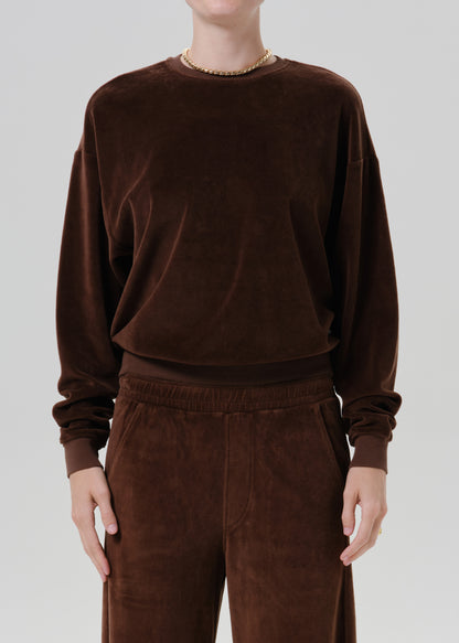 Woman wearing a dark brown crewneck sweatshirt with dark brown wide leg pants on a grey background.