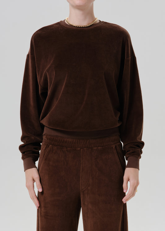 Woman wearing a dark brown crewneck sweatshirt with dark brown wide leg pants on a grey background.