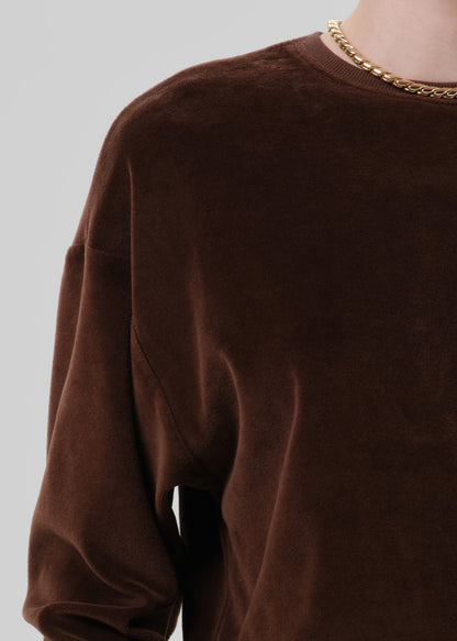 Close-up of a dark brown crewneck sweatshirt on a grey background.