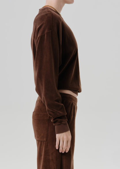 Woman wearing a dark brown crewneck sweatshirt with dark brown wide leg pants viewed from the side on a grey background.