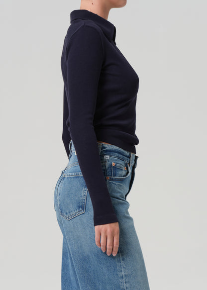 Person wearing a navy long-sleeve top and blue jeans on a light gray background
