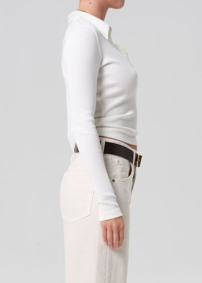 Person wearing a white long-sleeve top and light-colored pants on a plain background