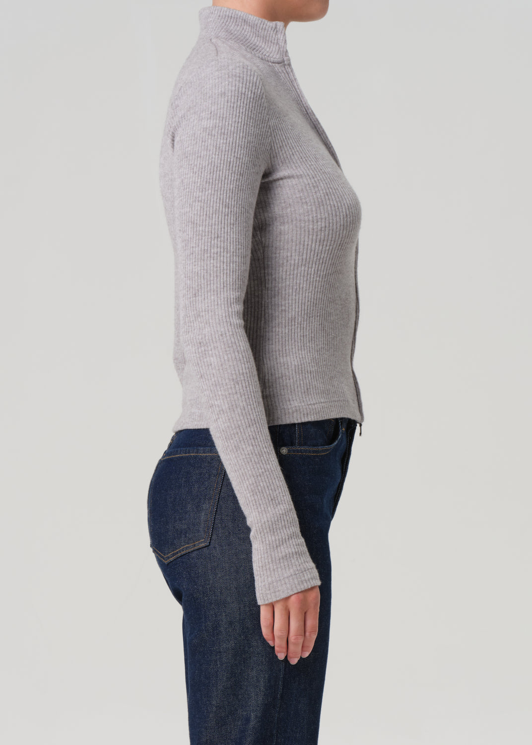 Person wearing a gray ribbed sweater and blue jeans on a light gray background
