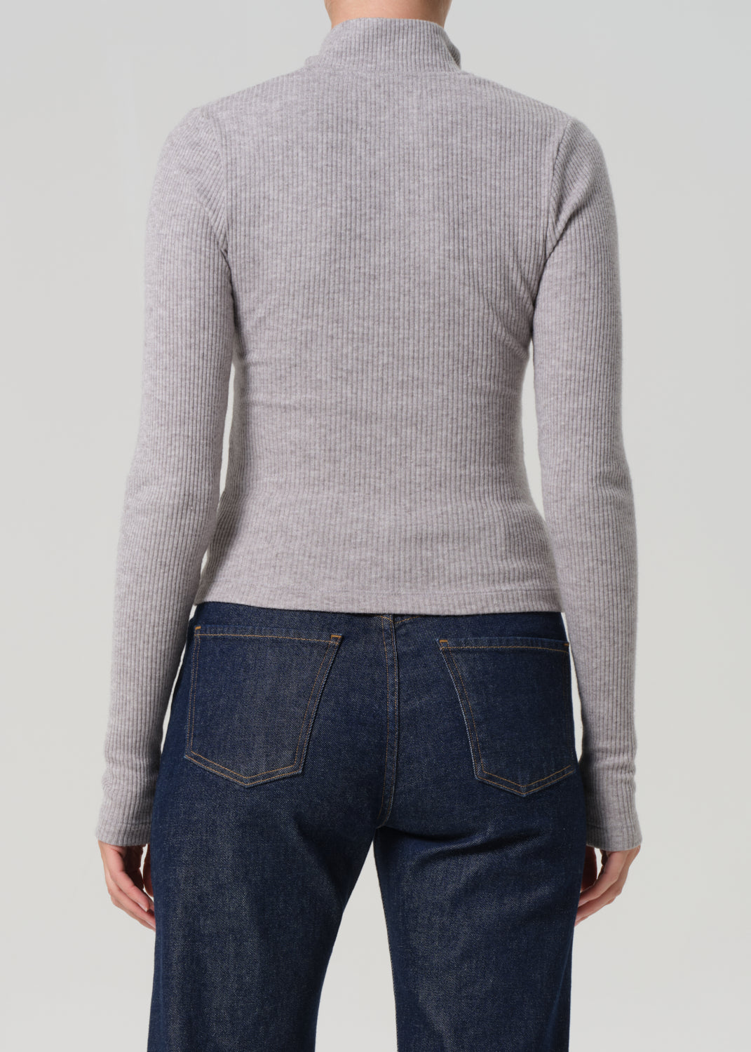 Person wearing a gray ribbed sweater and dark blue jeans on a light gray background