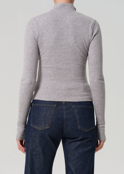 Person wearing a gray ribbed sweater and dark blue jeans on a light gray background