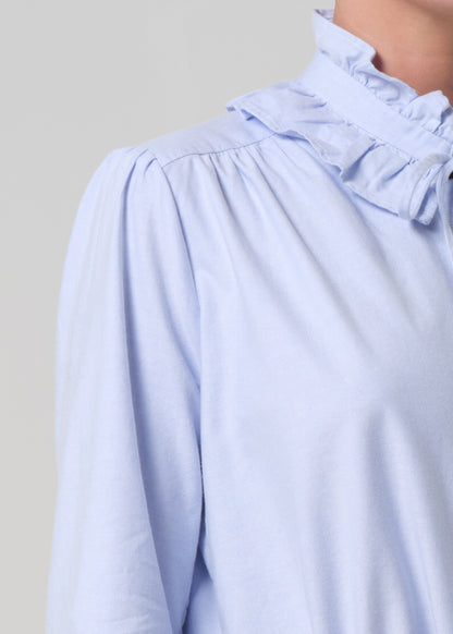 Light blue blouse with ruffled collar on a neutral background