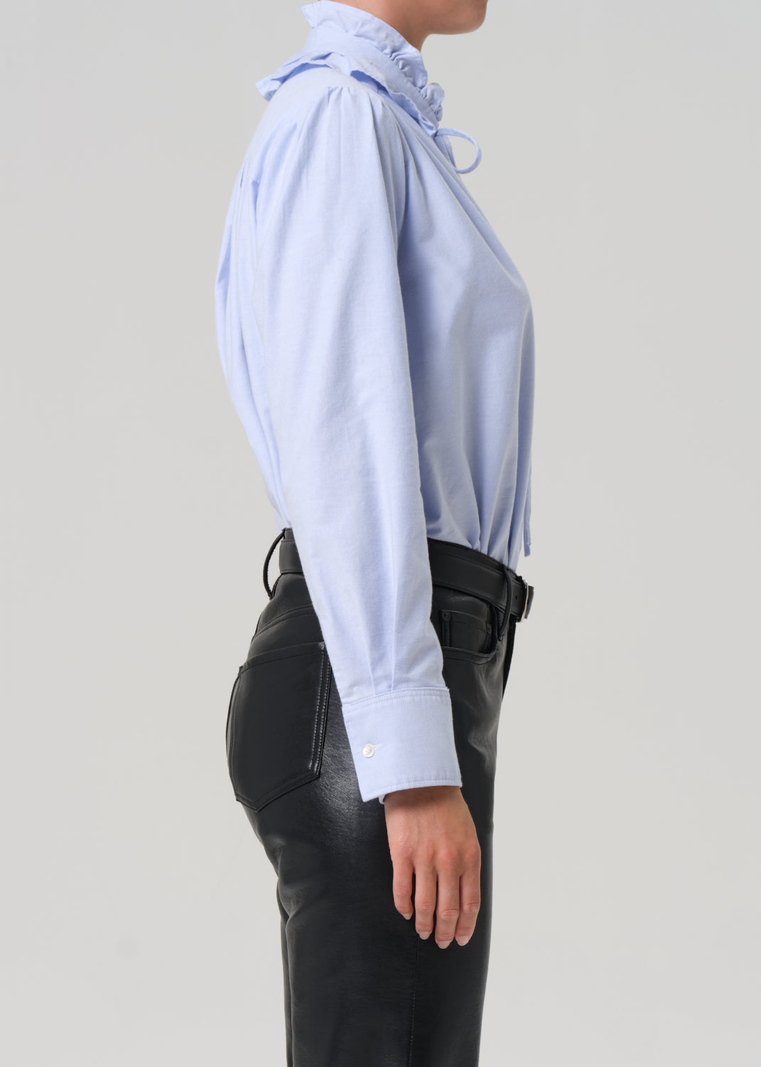 Person wearing a light blue shirt and black leather pants on a plain background