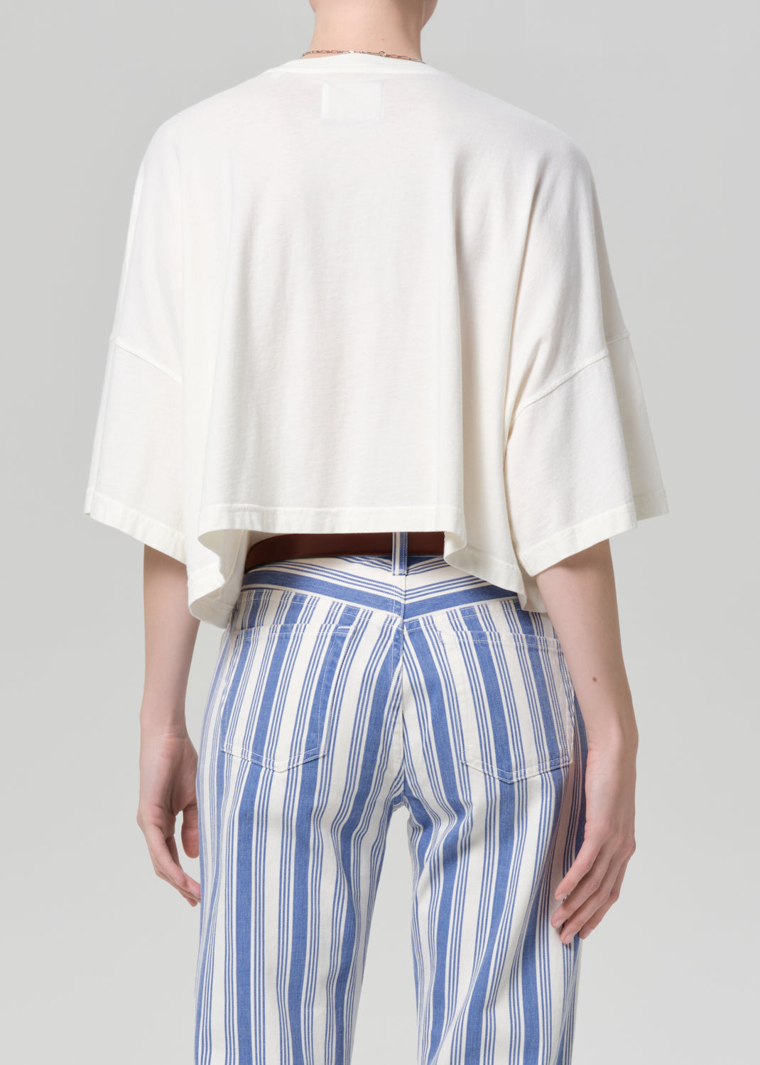 Person wearing a white top and blue striped pants on a gray background