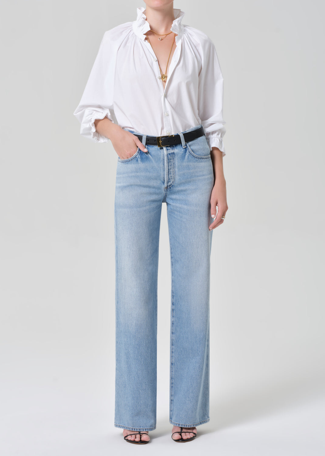 Person wearing a white shirt and light blue jeans on a plain background