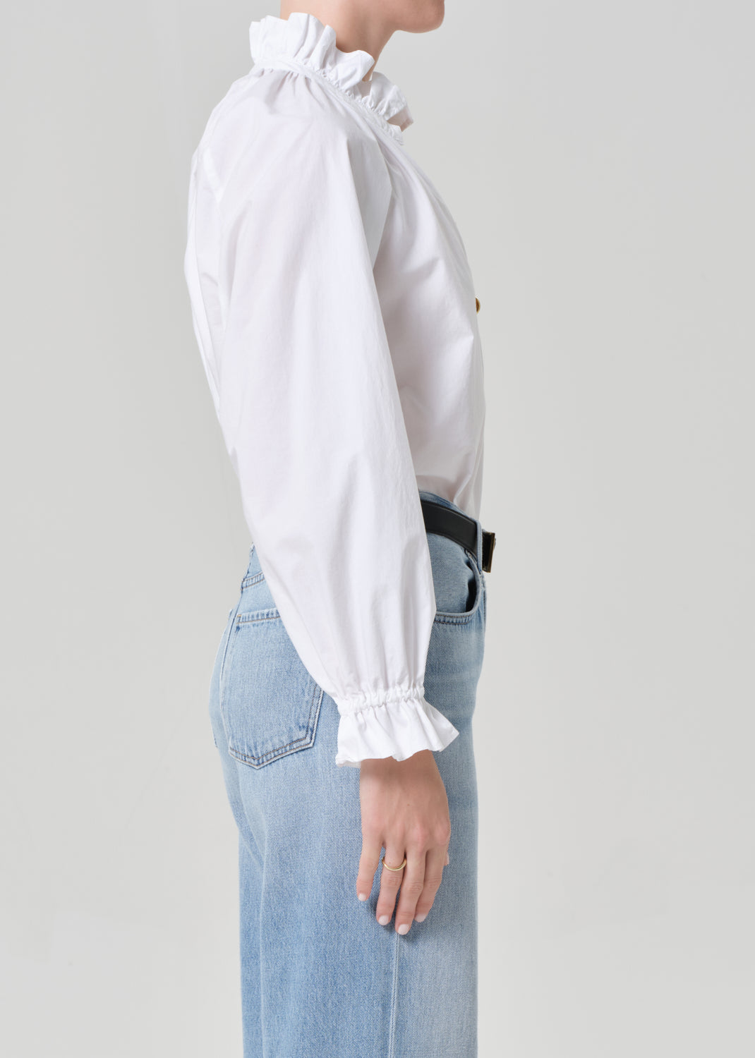 Person wearing a white blouse with ruffled sleeves and light blue jeans on a plain background