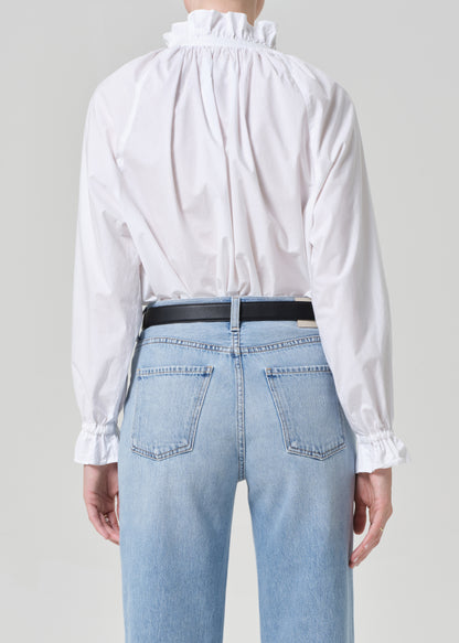 Person wearing a white blouse and light blue jeans with a plain background