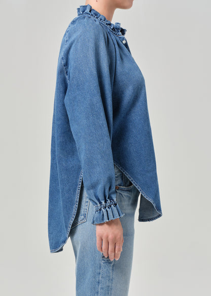 Blue denim shirt with ruffled details on a plain background