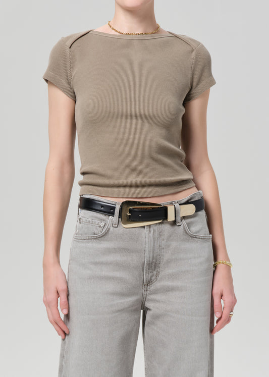 Person wearing a brown ribbed t-shirt and light gray jeans with a black belt on a plain background