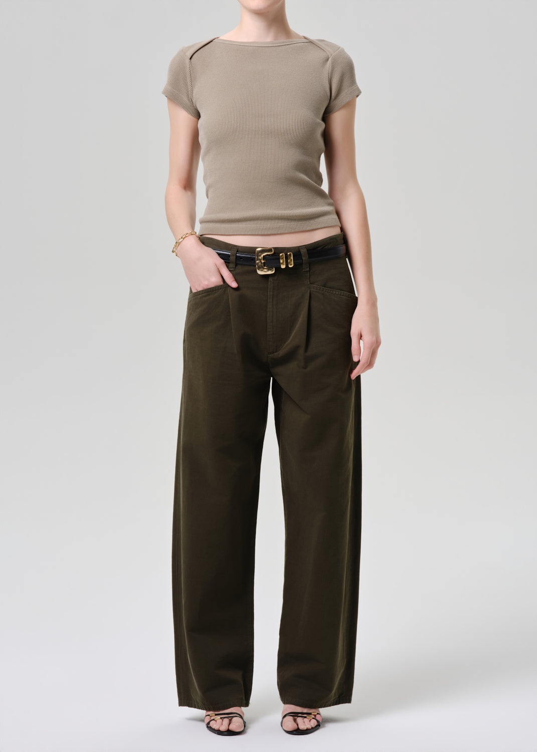 Person wearing a beige top and brown wide-leg pants on a grey background.
