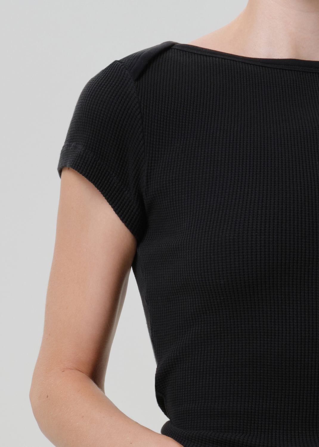 Close-up of a person wearing a black short-sleeve waffle-knit top against a light gray studio background.