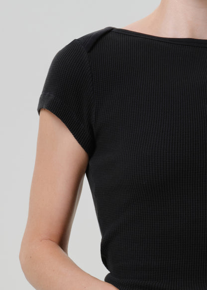 Close-up of a person wearing a black short-sleeve waffle-knit top against a light gray studio background.