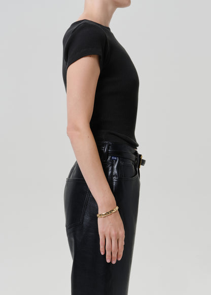 Side profile of a model wearing a black short-sleeve ribbed knit top and black leather pants against a light gray studio background.
