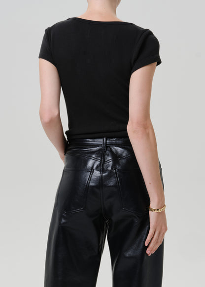 Rear view of a model wearing a black short-sleeve top and shiny black faux-leather pants against a light gray studio background.