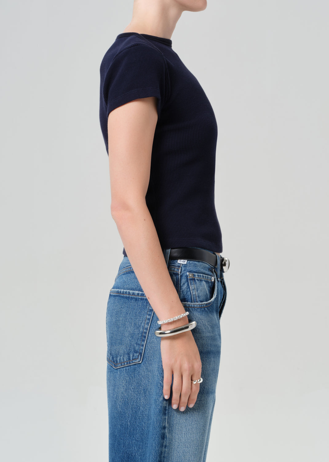Person wearing a navy top and blue jean shorts on a gray background