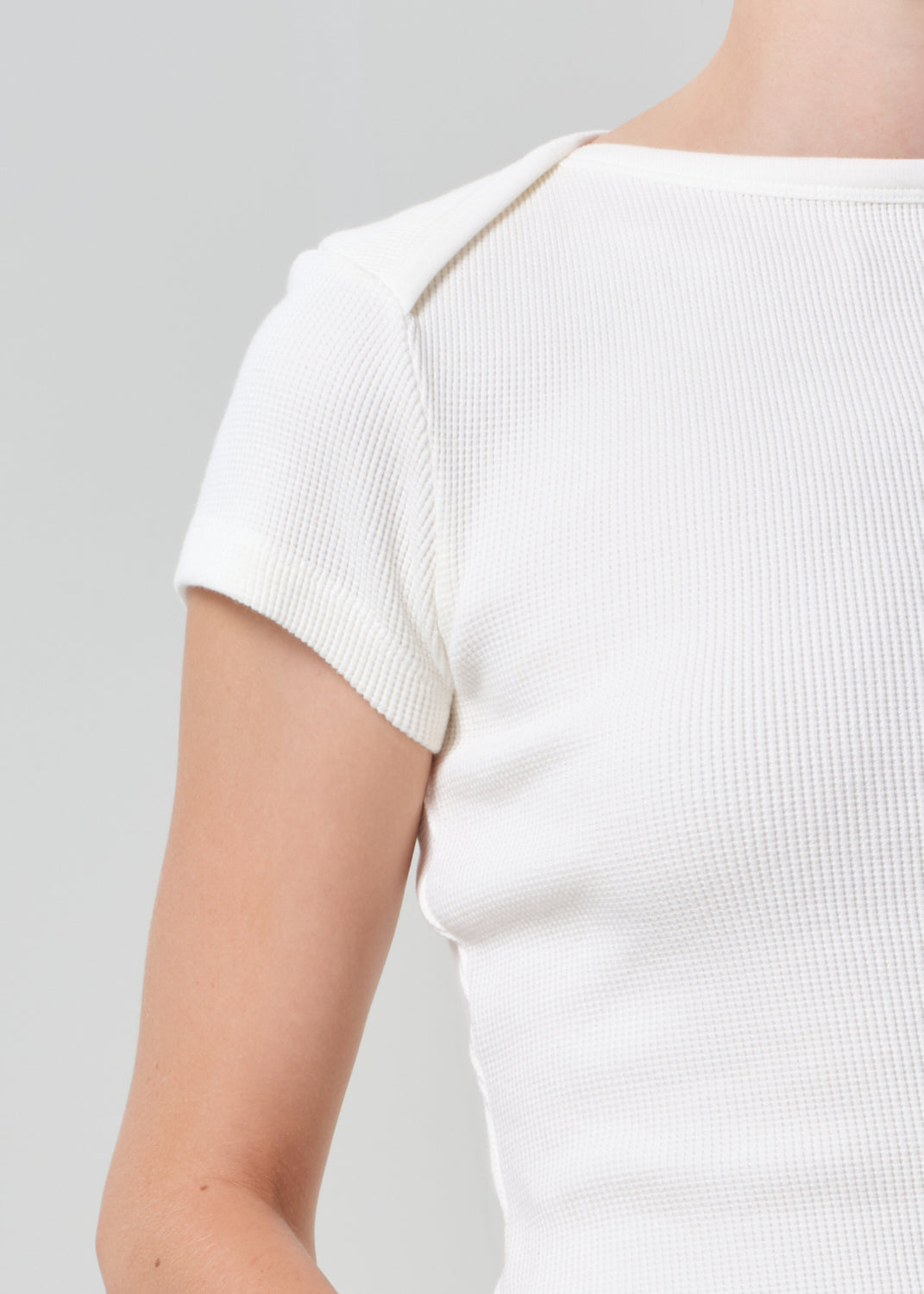 White ribbed knit top worn by a person on a gray background