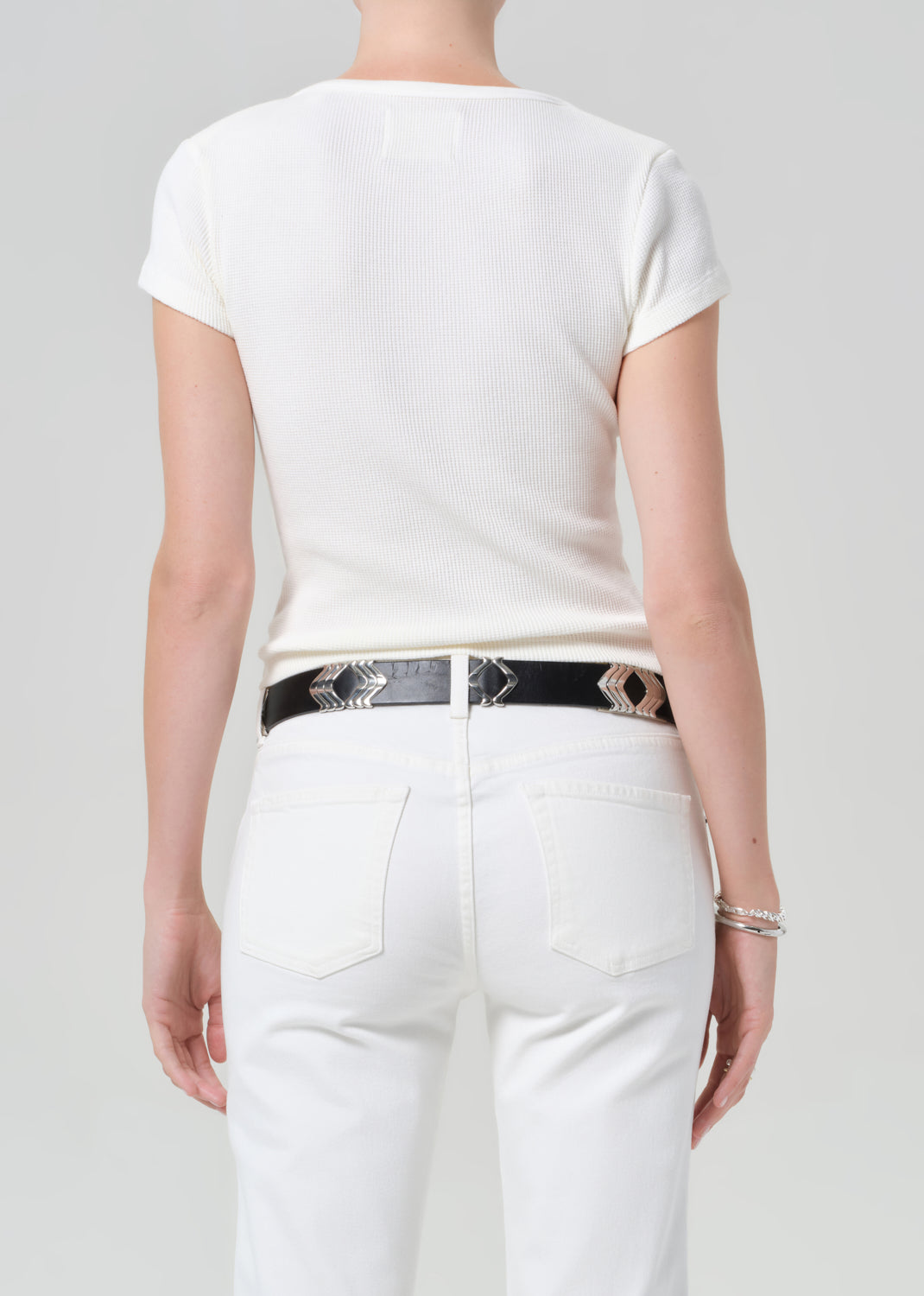 Person wearing a white t-shirt and white pants with a black belt featuring accents on a light gray background