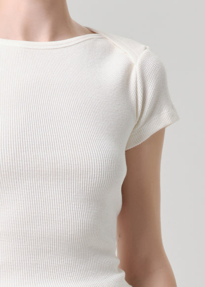 Close-up of a person wearing a short-sleeve waffle-knit top in off-white or cream, showing the textured fabric and shoulder area against a grey background.
