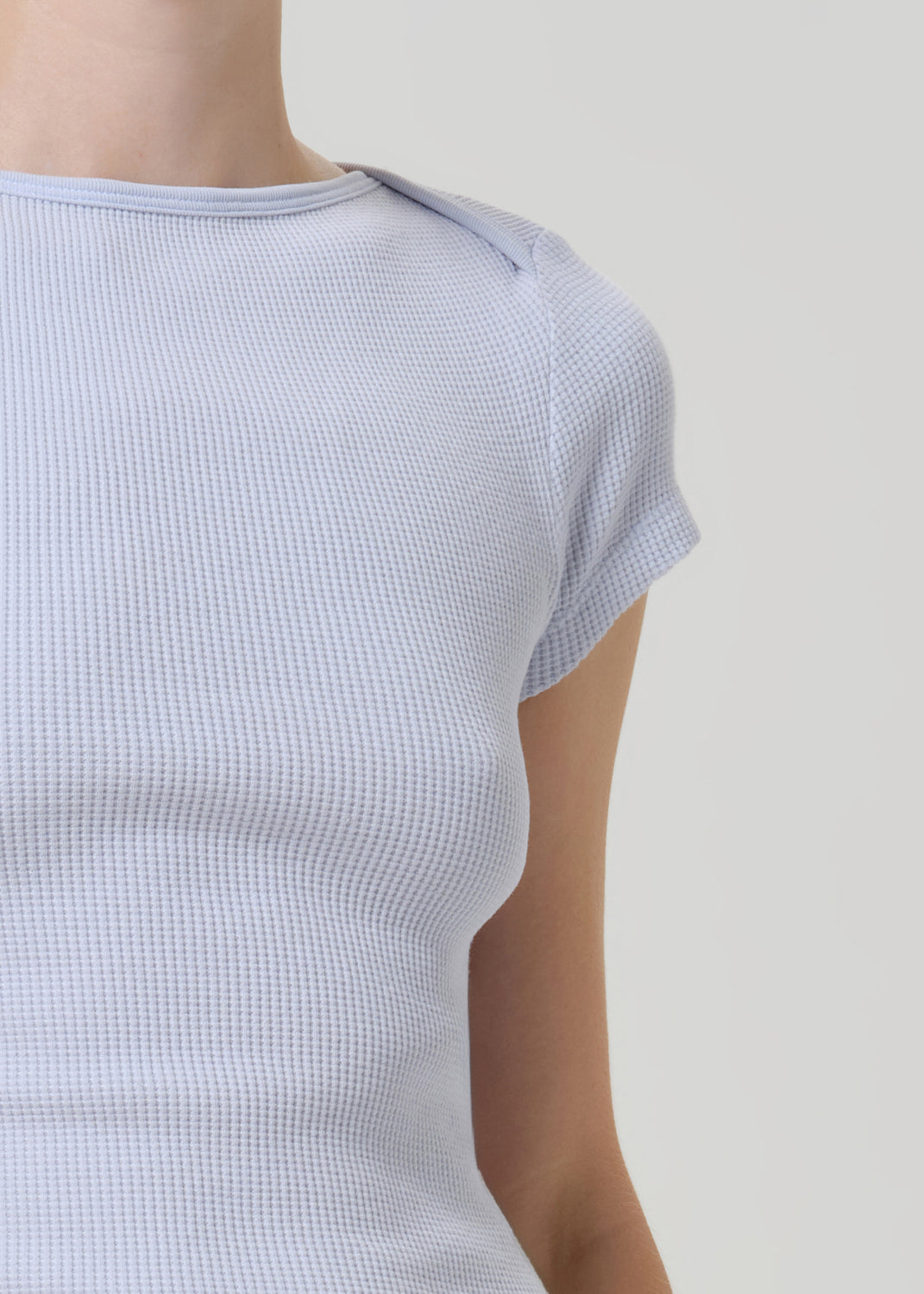 Close-up of a person wearing a light blue waffle-knit short-sleeve top against a plain light gray background.