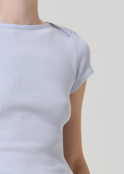 Close-up of a person wearing a light blue waffle-knit short-sleeve top against a plain light gray background.