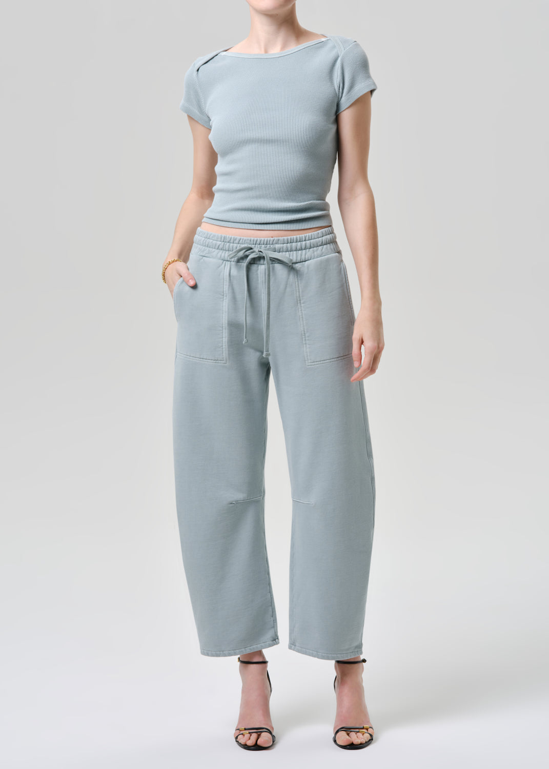 Person wearing a light blue outfit with a top and wide-leg pants on a grey background
