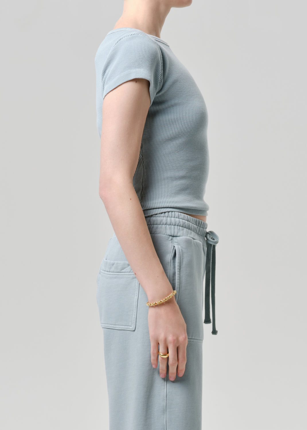 Person wearing a light gray ribbed sweater and pants on a grey background