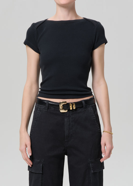 Person wearing a black top and black pants with a gold belt on a gray background