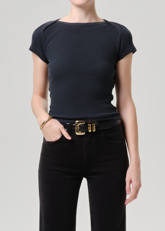 A model wearing a dark navy ribbed short-sleeve boat-neck top tucked into black jeans with a gold buckle belt, shot against a grey background.