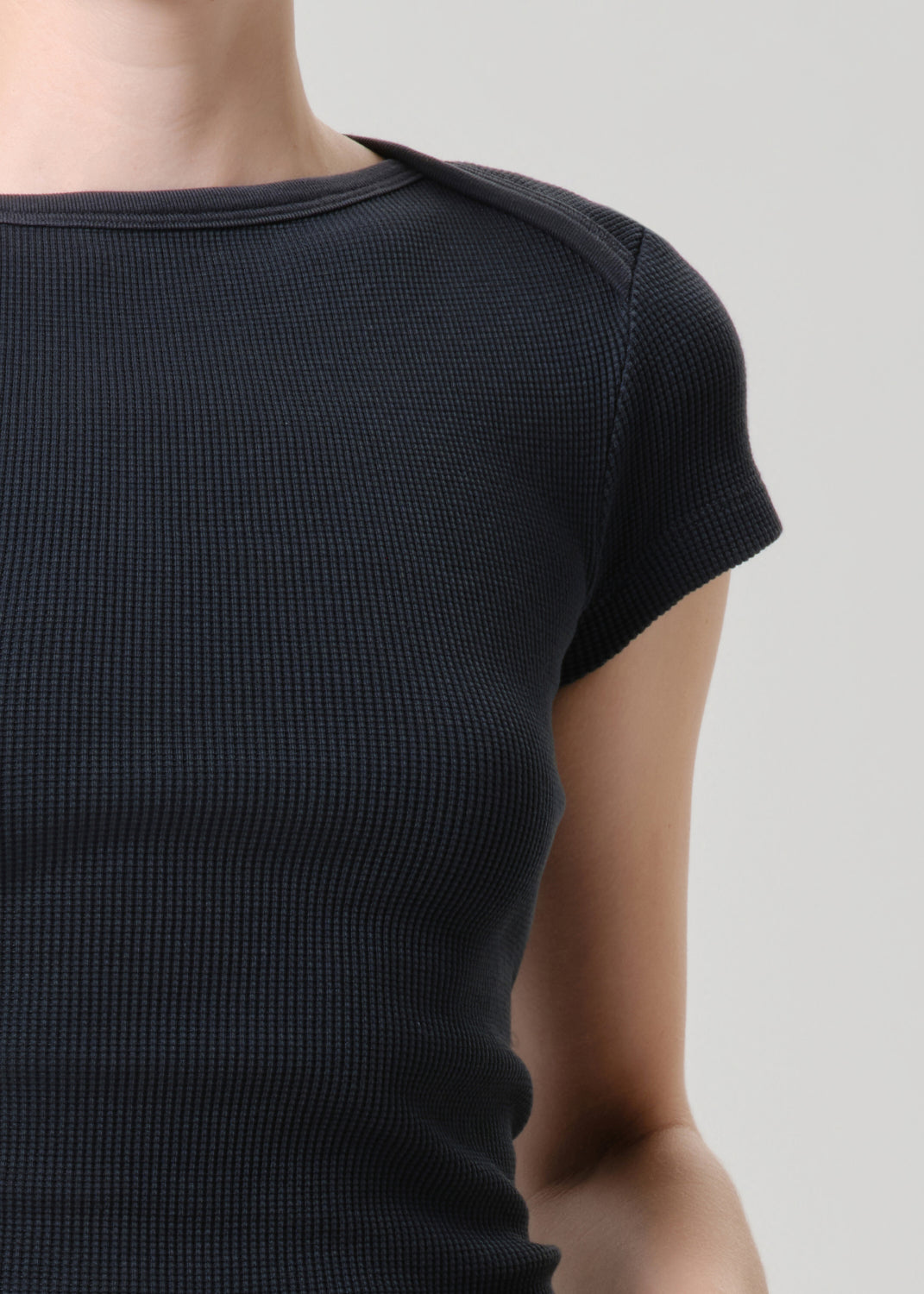 Close-up of a person wearing a dark navy ribbed short-sleeve top against a grey background.