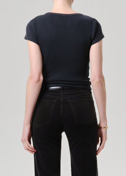 A model wearing a dark navy ribbed short-sleeve top tucked into black jeans with a gold buckle belt, shot against a grey background.