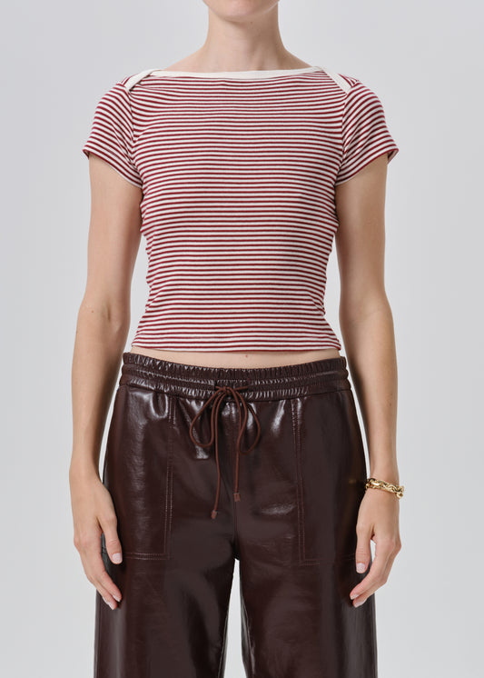 A model wearing a short-sleeve striped knit top with red and white horizontal stripes, paired with dark brown faux-leather pants, against a grey background.