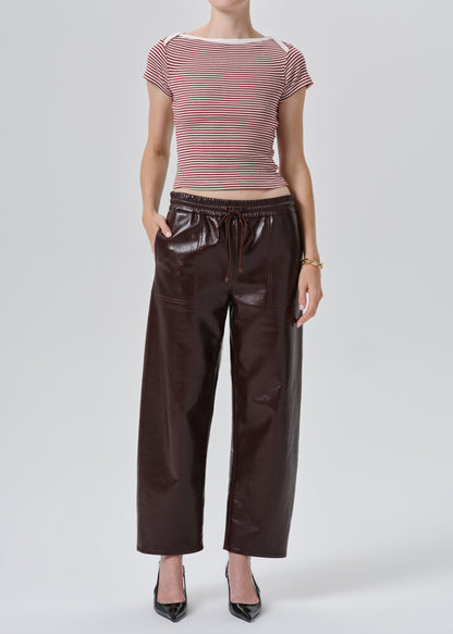 A model wearing a pink and white striped short-sleeve top and dark brown faux-leather wide-leg pants, paired with black pointed-toe heels, against a grey background.