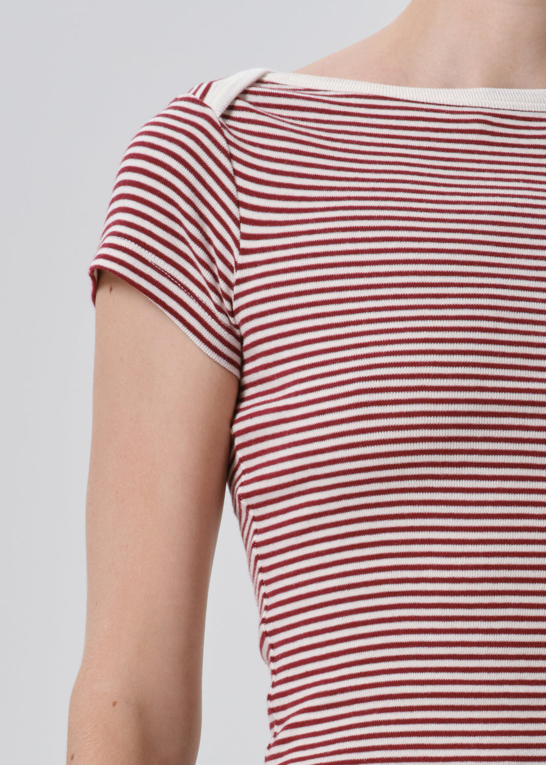 Close-up of a person wearing a short-sleeve ribbed top with horizontal red and off-white stripes, cropped from the neck to the upper torso against a grey background.
