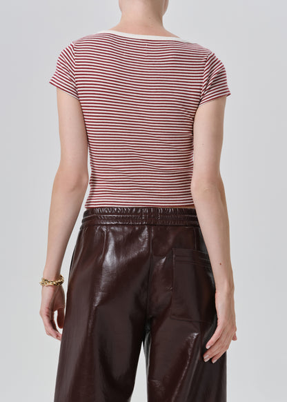 Rear view of a model wearing a short-sleeve crew-neck top with thin red and white horizontal stripes, paired with dark brown faux-leather pants, against a grey background.