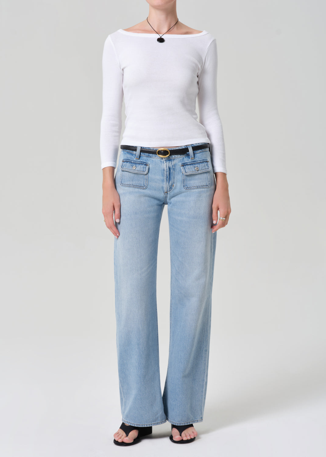 Person wearing a white long-sleeve top and light blue jeans on a plain background