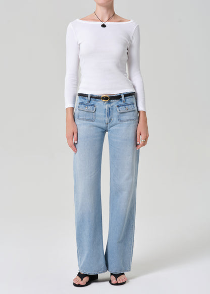 Person wearing a white long-sleeve top and light blue jeans on a plain background