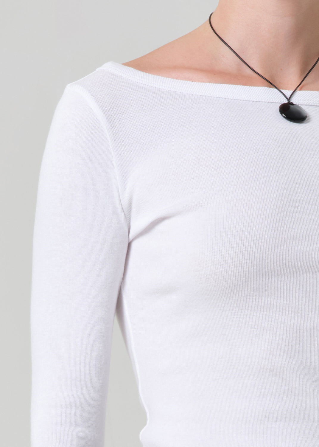 Person wearing a white long-sleeve top with a black necklace on a plain background