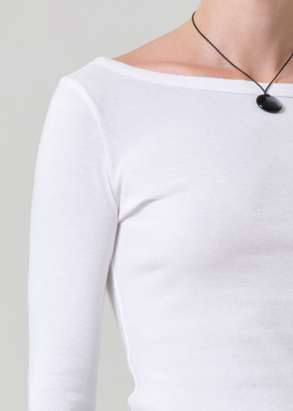 Person wearing a white long-sleeve top with a black necklace on a plain background