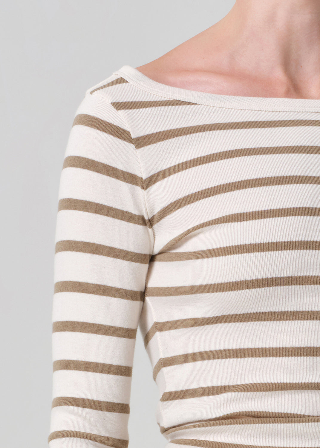 Close-up of a person wearing a white long-sleeve shirt with brown horizontal stripes on a gray background.