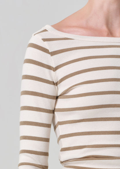 Close-up of a person wearing a white long-sleeve shirt with brown horizontal stripes on a gray background.