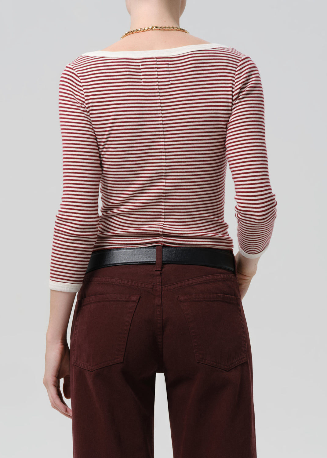 Person wearing a red and white striped shirt with maroon pants on a grey  background