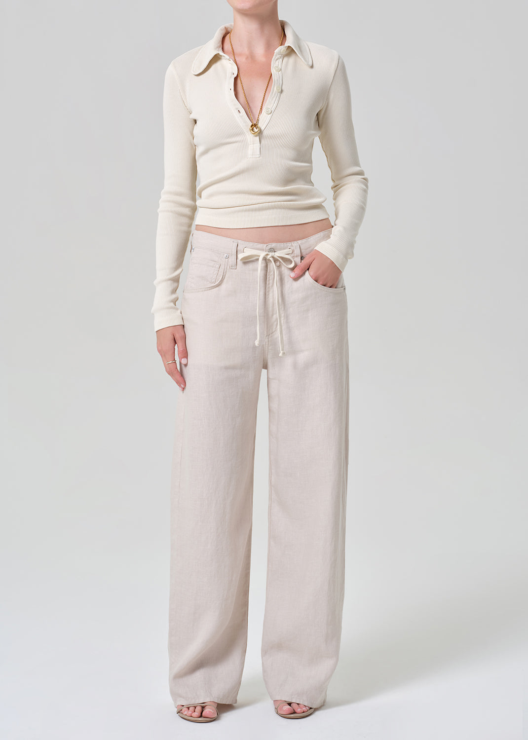 Person wearing a cream-colored long-sleeve shirt and light-colored pants on a plain background