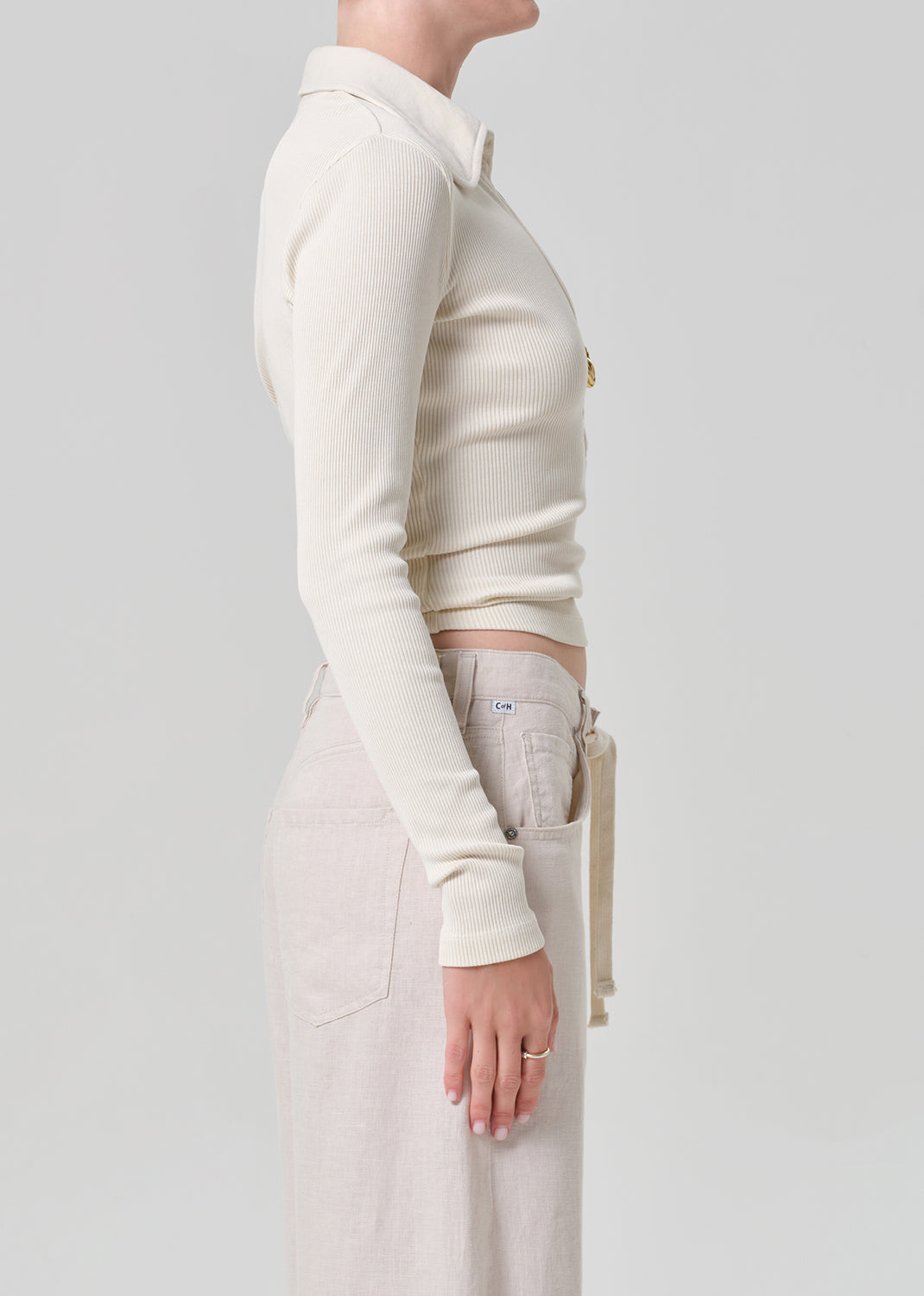 Person wearing a cream-colored long-sleeve shirt and light-colored pants on a plain background