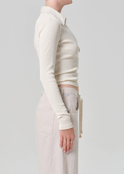 Person wearing a cream-colored long-sleeve shirt and light-colored pants on a plain background