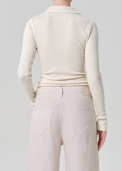 Person wearing a cream-colored long-sleeve shirt and light-colored pants on a plain background