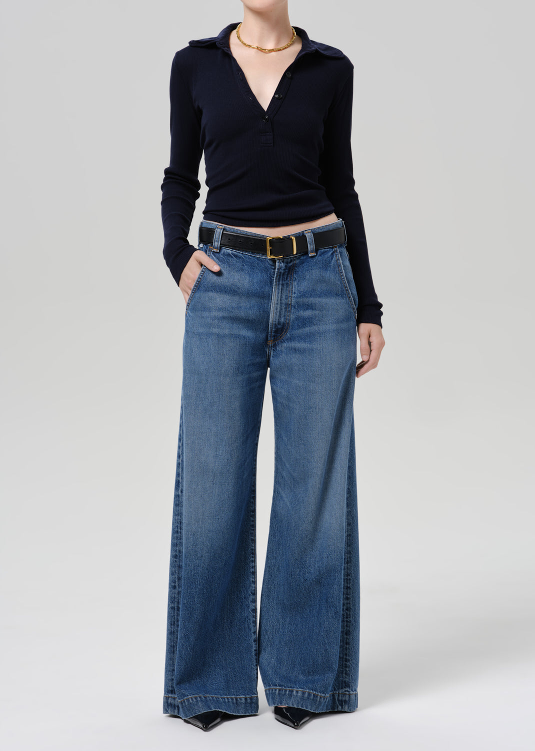 Person wearing blue polo sweater and blue pants on a grey background